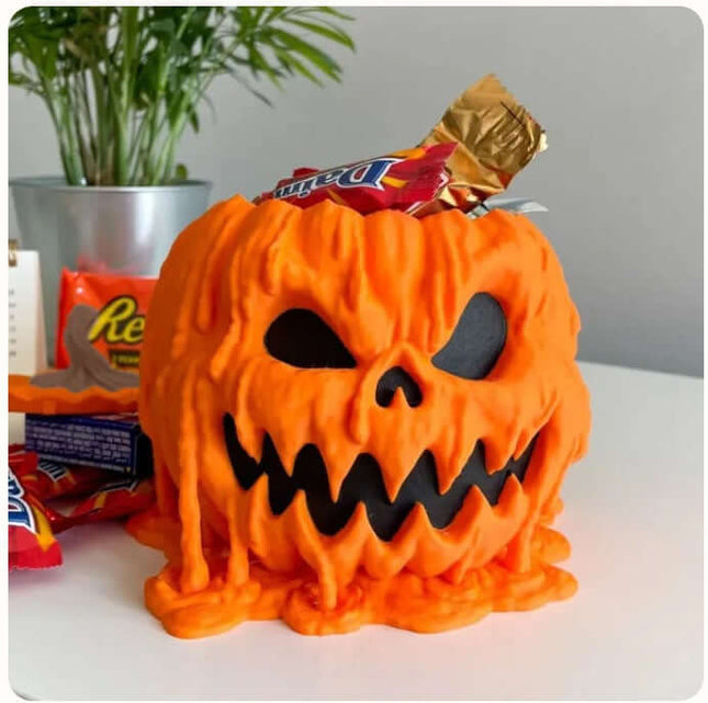 Halloween Melting Pumpkin Candy Bowl With Lid filled with assorted candies on a table with green foliage in the background.