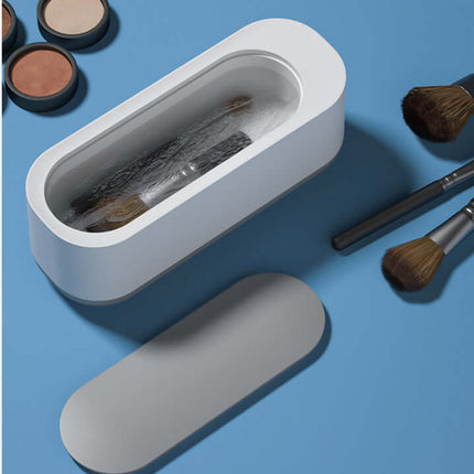 Ultrasonic High Frequency Jewelry and Glasses Cleaner with makeup brushes and cosmetics on a blue surface.