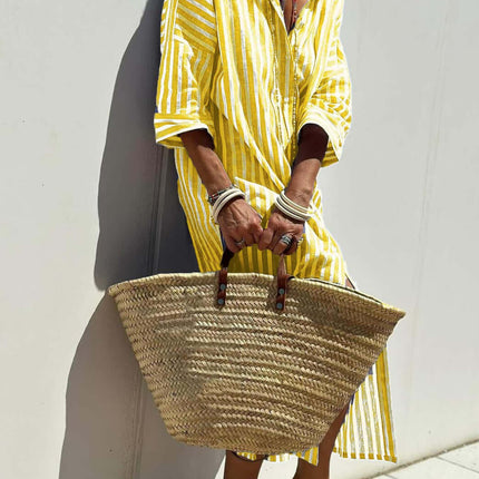 A woman wearing a Striped Half-Sleeve Belted Lapel Shirt Dress in yellow, holding a straw tote bag.