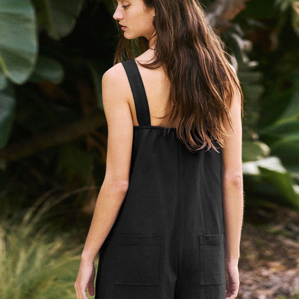 Back view of a woman wearing a Womens Casual Solid Color Short Jumpsuit Romper in black, surrounded by greenery.